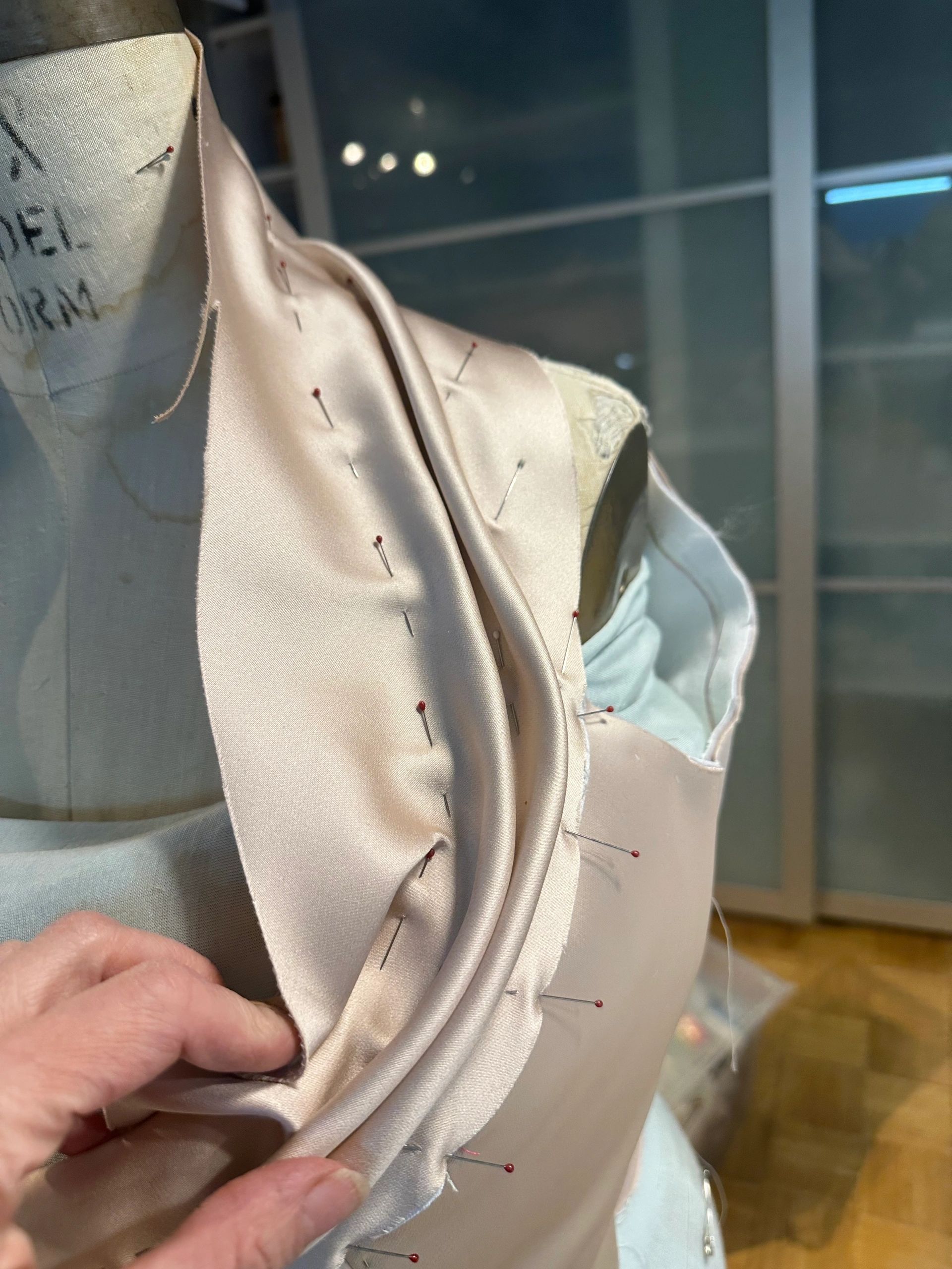 Tailoring satin fabric pinned on a dress form.