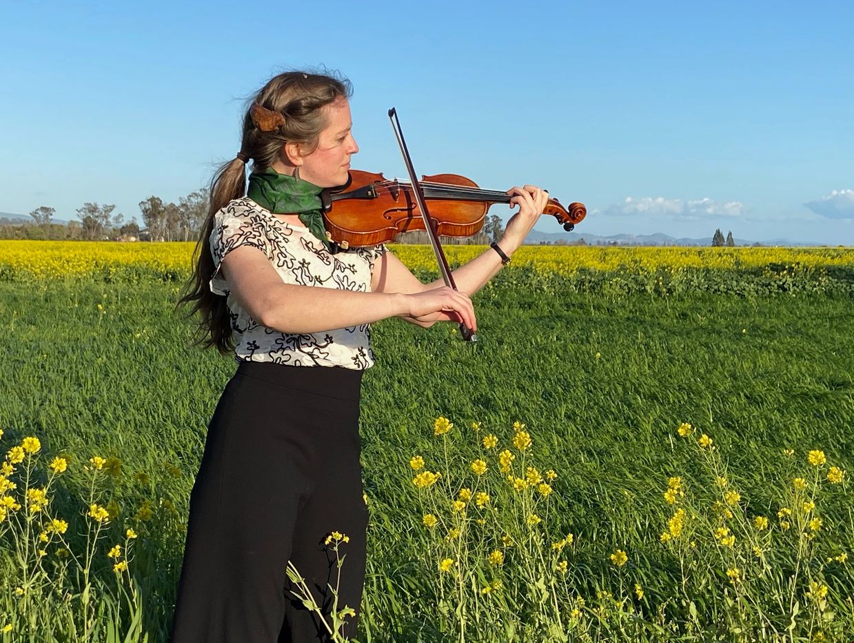 Katrina playing violin in a field with yellow flowers.