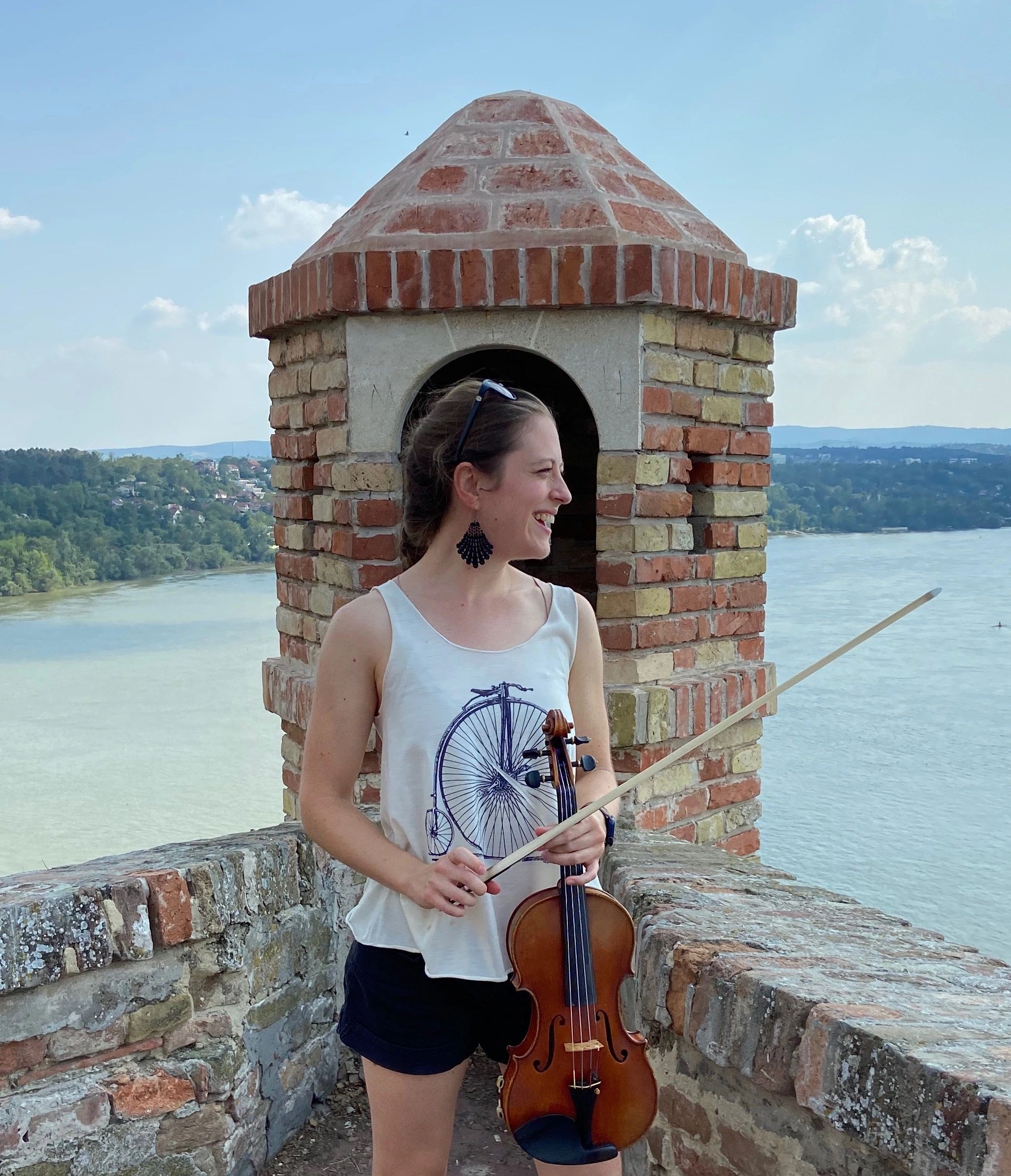 Katrina with violin in front of tower and river in Novi Sad, Serbia