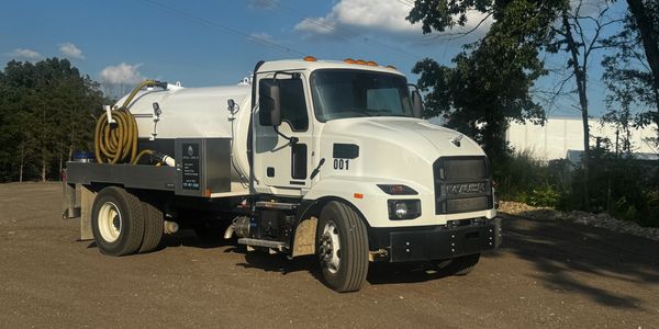 White Mack vacuum truck parked on dirt under a partly cloudy sky.