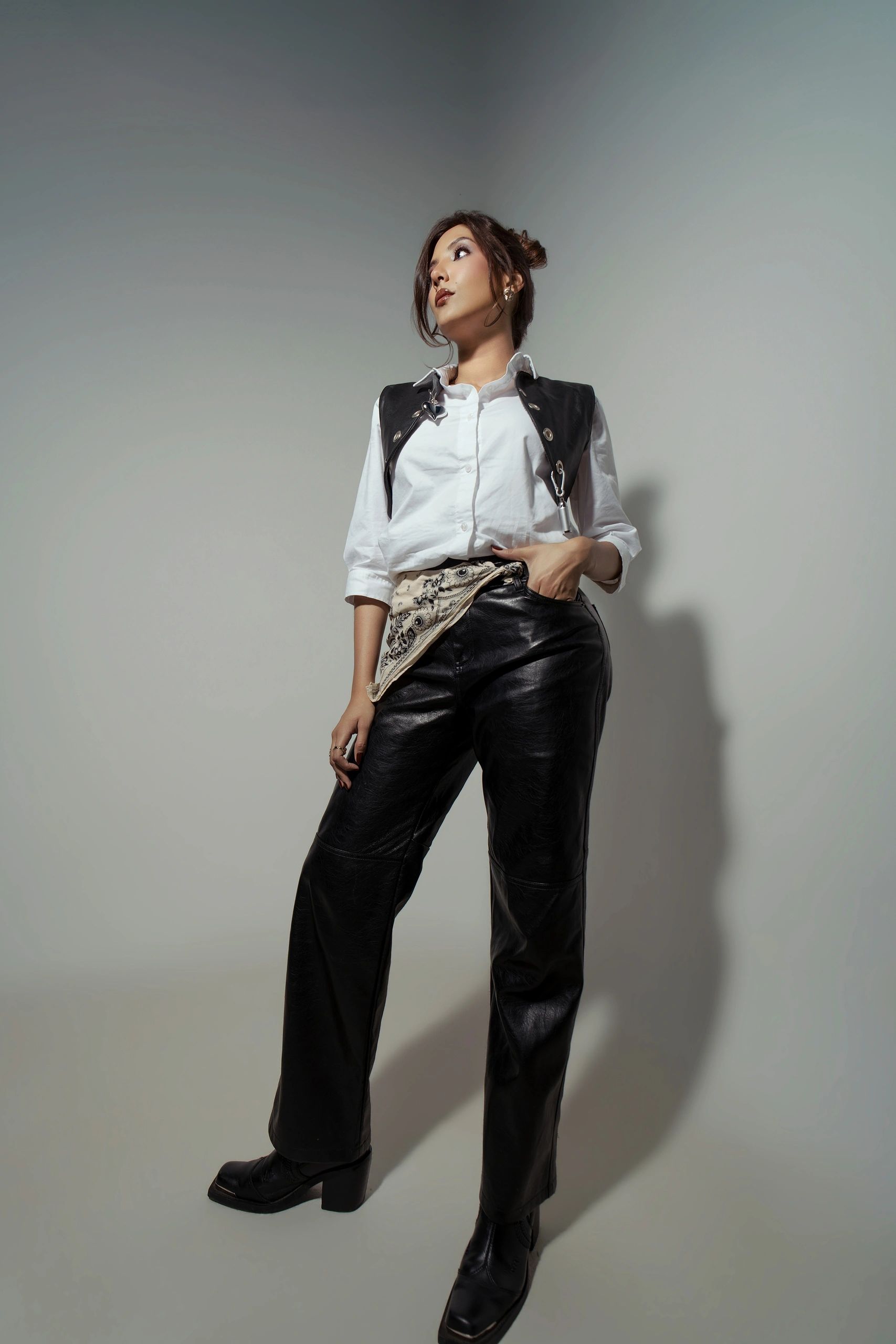 Confident woman posing in stylish black leather pants and white shirt with a black vest.