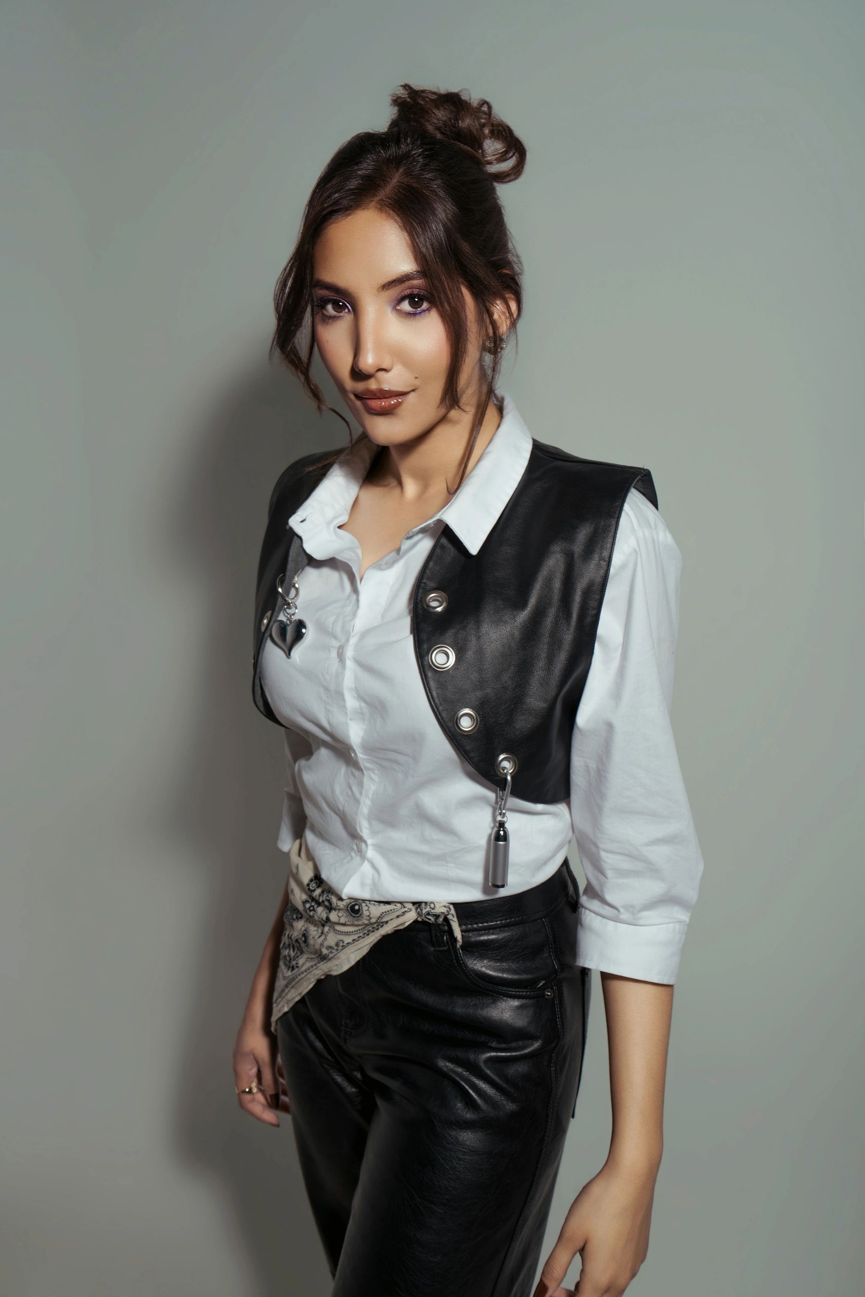 Stylish woman in white shirt and black leather vest posing confidently.