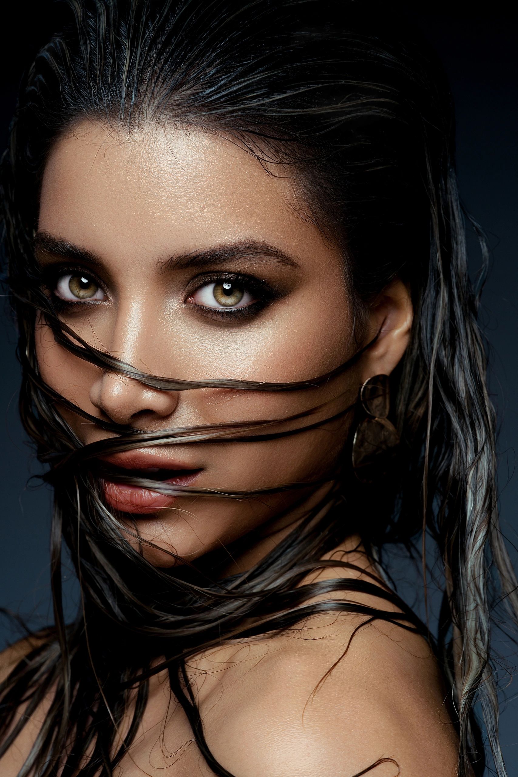 Close-up portrait of a woman with wet hair partially covering her face and striking eyes.