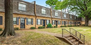 Row of brick townhouses with trees and a small bridge.