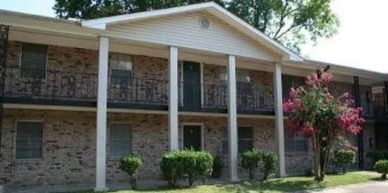 Two-story brick apartment building with columns and greenery.