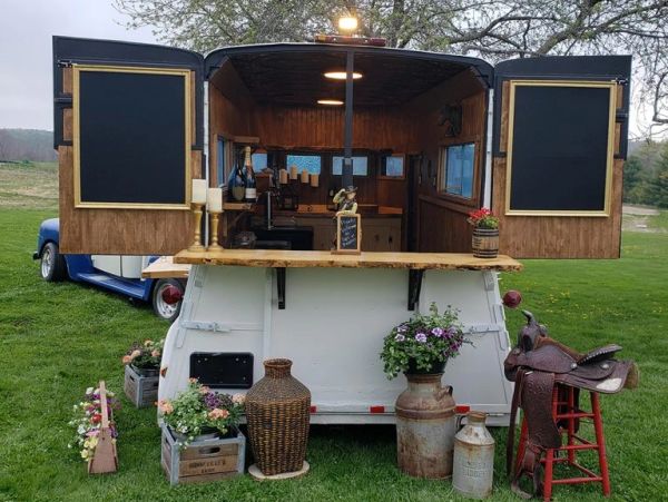 A mobile rustic bar set up in a white trailer with wooden interior.