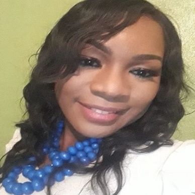Smiling woman with wavy hair and blue beaded necklace.