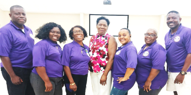 Group of seven people smiling, mostly wearing purple shirts.