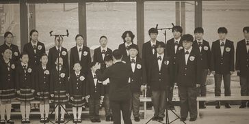 A school choir performs under a conductor's direction in a vintage-style photo.