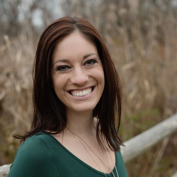 A woman with a bright smile wearing a green top and layered necklaces.