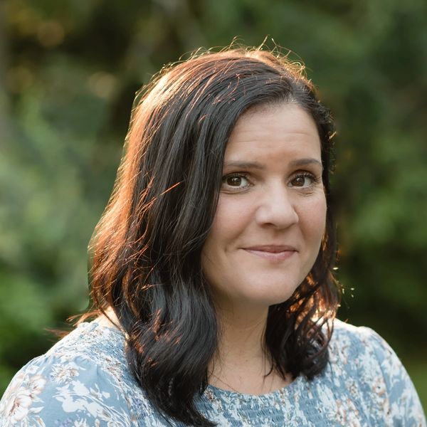 A woman with dark hair wearing a floral blue dress outdoors.