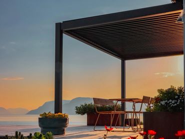 Sunset view from a modern patio overlooking the ocean with chairs and plants.
