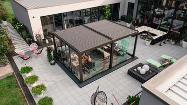 Modern glass sunroom with seating in a spacious patio area.