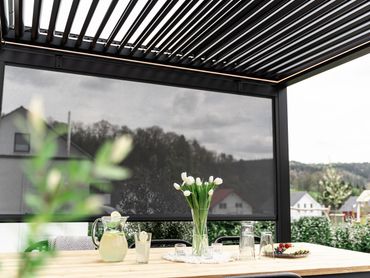 Outdoor patio with a modern pergola and a vase of white tulips on the table.