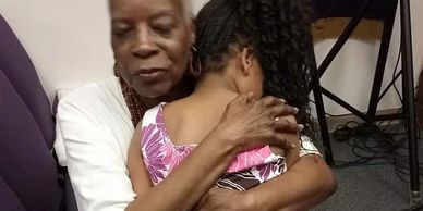 founder Bonnie Harrison hugging a black child sitting in her lap with their head on her shoulder