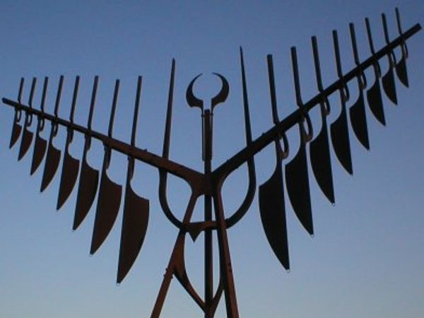 Metal sculpture resembling a large, winged figure against a dusky sky.