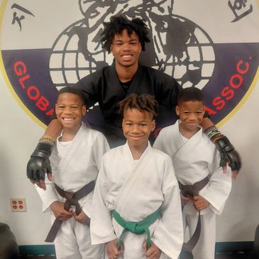 Martial arts instructor with three young students in uniforms and belts.