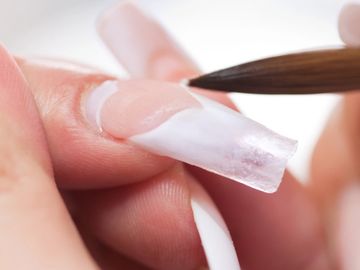 Applying gel nail extension with a brush on a fingernail.