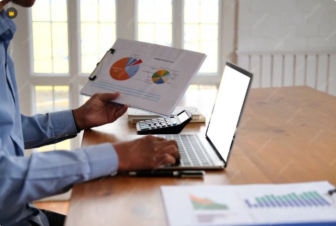 Person analyzing pie charts and graphs on a laptop and clipboard.