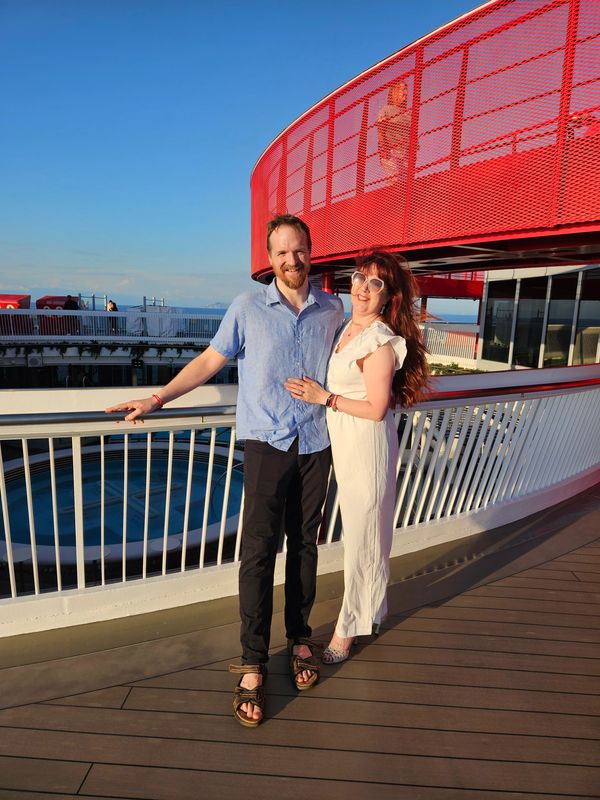 Couple smiling next to railing on sunny deck.