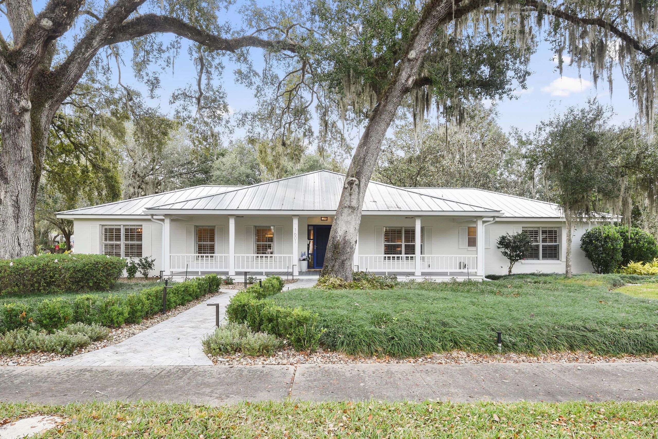 White house with a metal roof and large trees in front.