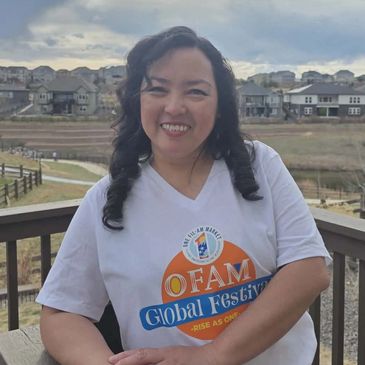 Woman in OFAM Global Festival t-shirt smiling outdoors on a balcony.