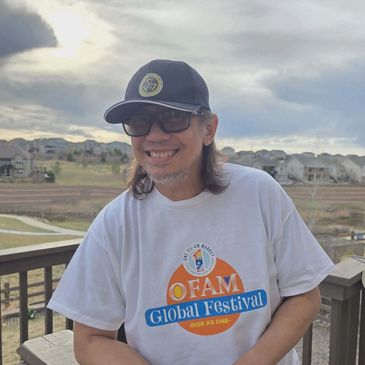 Man smiling outdoors wearing a Global Festival t-shirt and cap.