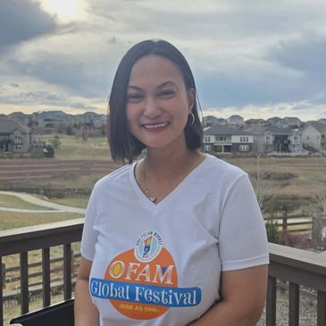 Woman smiling outdoors wearing an OFAM Global Festival t-shirt.