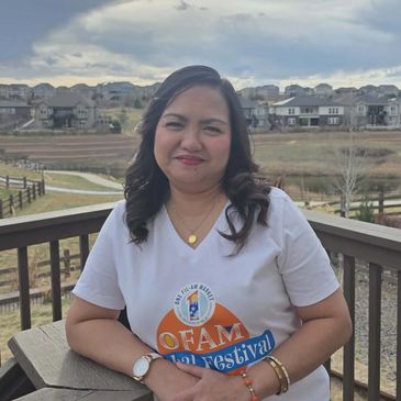 Woman smiling on a balcony wearing an OFAM festival t-shirt.