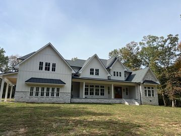 Large modern farmhouse with white siding and stone accents under a clear sky.
