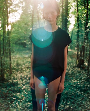 Person standing in a sunlit forest with lens flare.