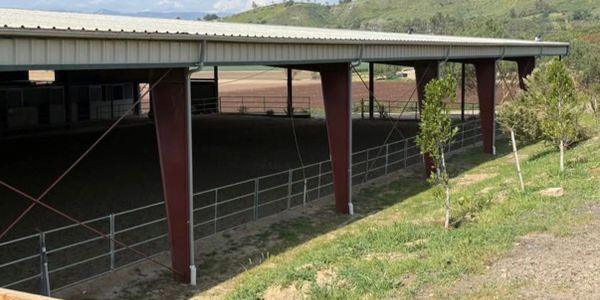 Large covered outdoor arena with metal supports and fencing.
