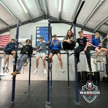 A group of young athletes sitting on gym equipment bars inside a training facility.