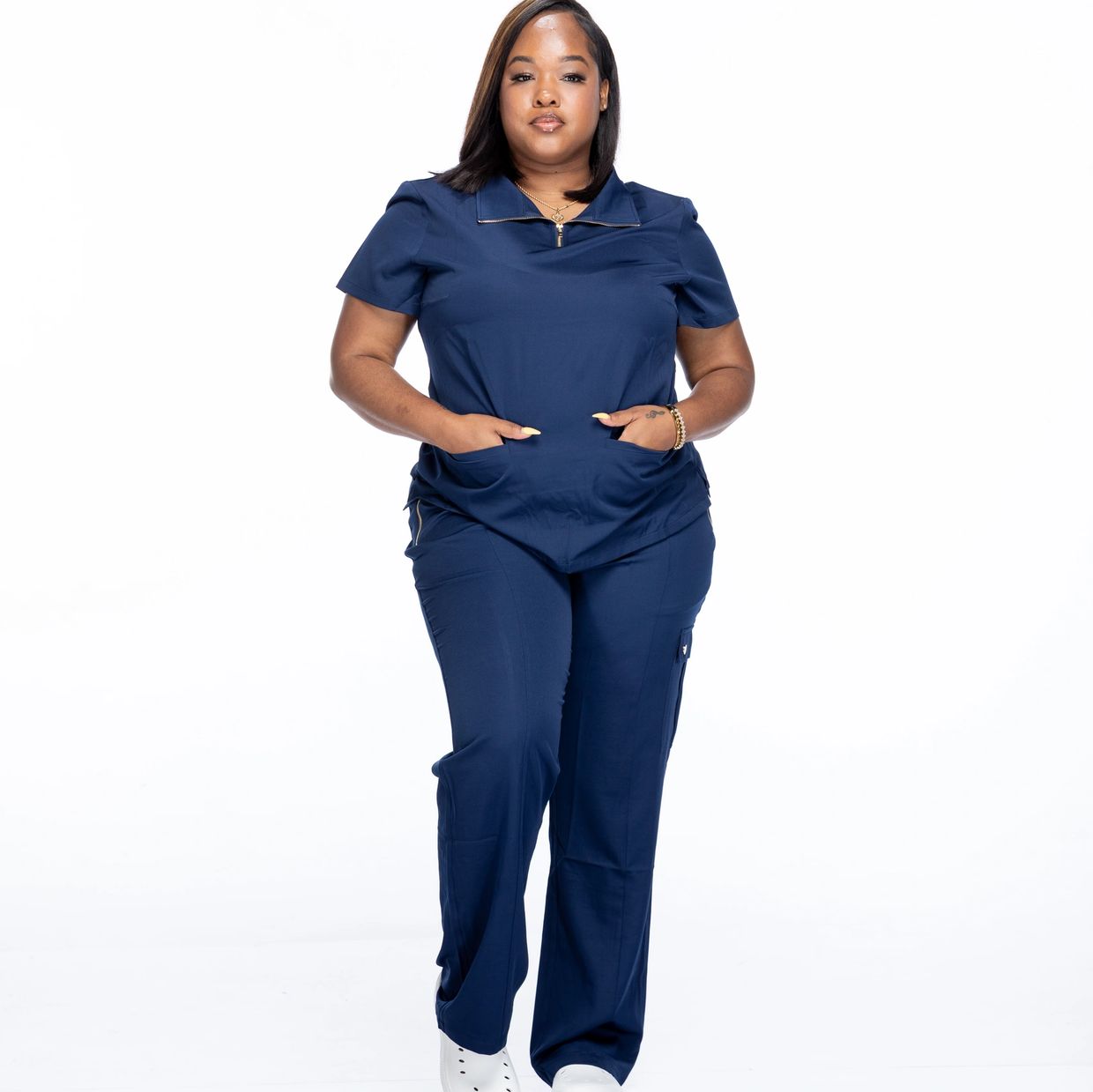 Confident woman in navy blue scrubs posing with hands in pockets.