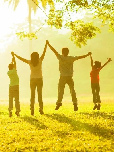 A family joyfully jumps holding hands in a sunlit park.