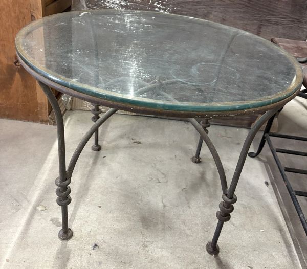 Round glass tabletop with a metal frame and legs, showing signs of wear.