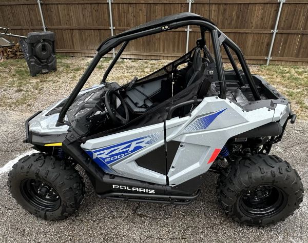 Silver Polaris RZR 200 EFI off-road vehicle parked on gravel.
