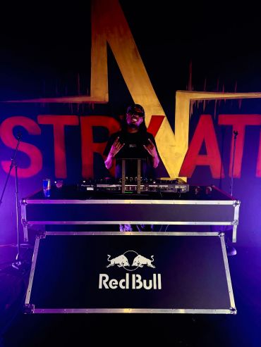 DJ performing at a Red Bull event with vibrant lighting.