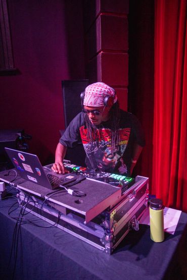 DJ performing with laptop and mixer in a dimly lit setting.
