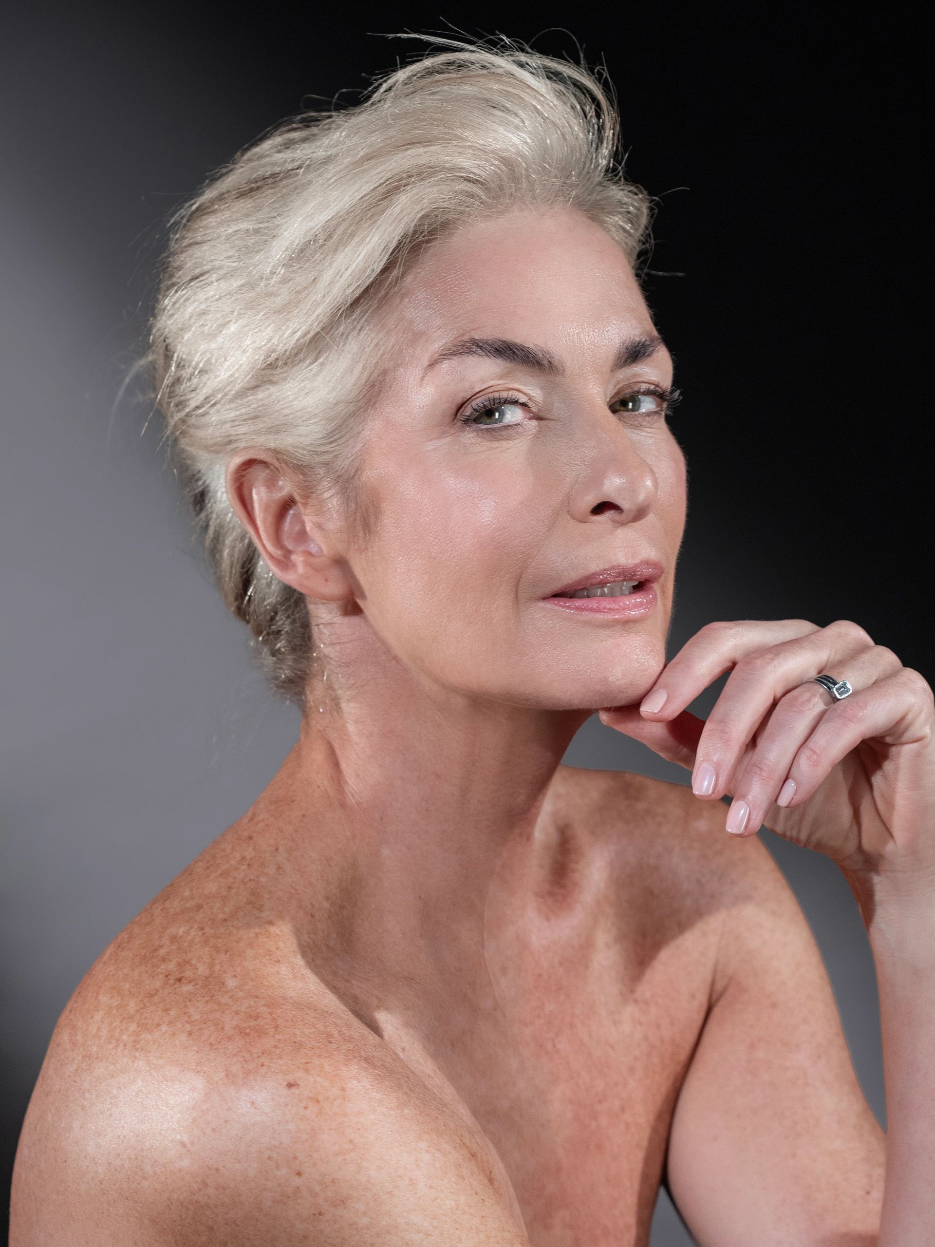 Confident mature woman with silver hair posing thoughtfully against a dark background.