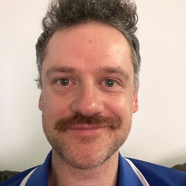 Smiling man with a mustache and curly hair.