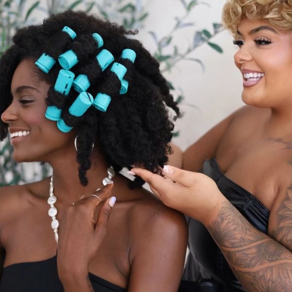 Hair stylist curling a woman's natural hair with blue rollers.