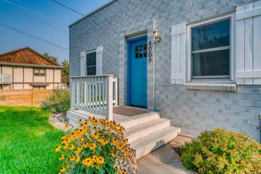 Front entrance of a gray house with a bright blue door and yellow flowers.