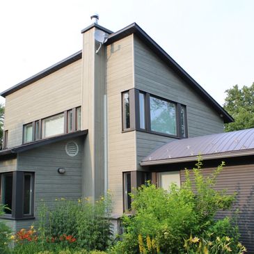 Modern two-story house with large windows and greenery.