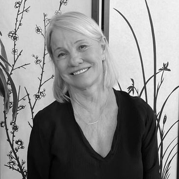 Smiling elderly woman with light hair in front of a decorative screen.