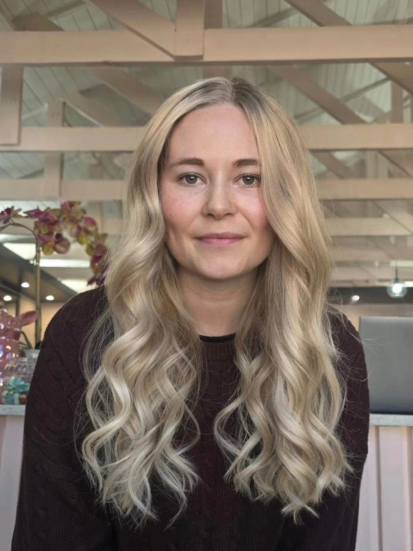 Smiling woman with long wavy blonde hair indoors under wooden beams.