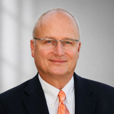 Smiling middle-aged man in glasses wearing a suit and orange tie.