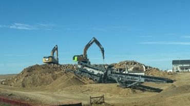 Construction site with excavators and soil piles under a clear sky.