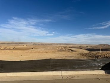 A barren construction site under a partly cloudy blue sky.