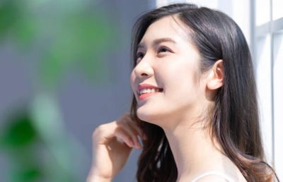 A young woman smiling softly by a window with sunlight.
